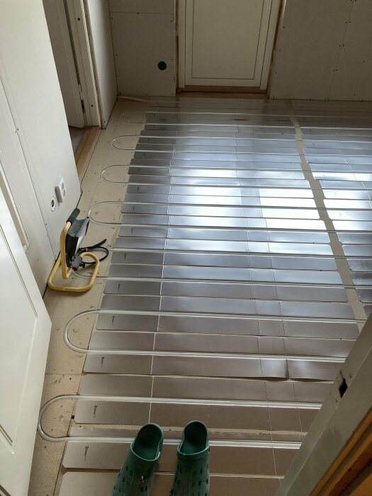 Installation av golvvärme under golvgips med synliga värmeslingor och verktyg på ett nyrenoverat golv.