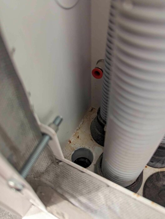Fuktigt område och fingeravtryck nära ett skvallerrör och rörledningar bakom tvättmaskin.