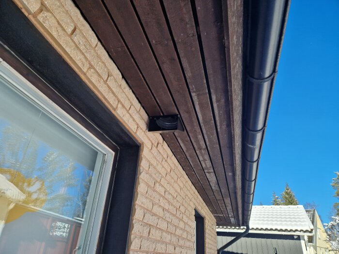 Installation av en svart spirokanal längs brunmålat taklutning med stenhusvägg i bakgrunden.