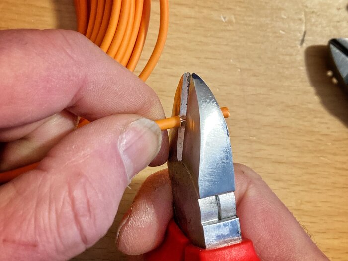 Händer som använder en Jokari skaltång för att skala slutet av en orange kabel.