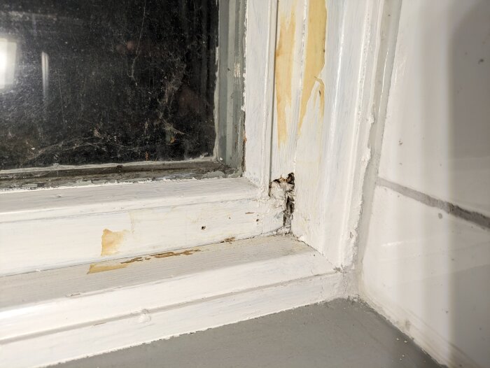 Slitet fönsterhörn med skador i fogen och vitmålade fönsterkarmar, behov av underhåll synligt.