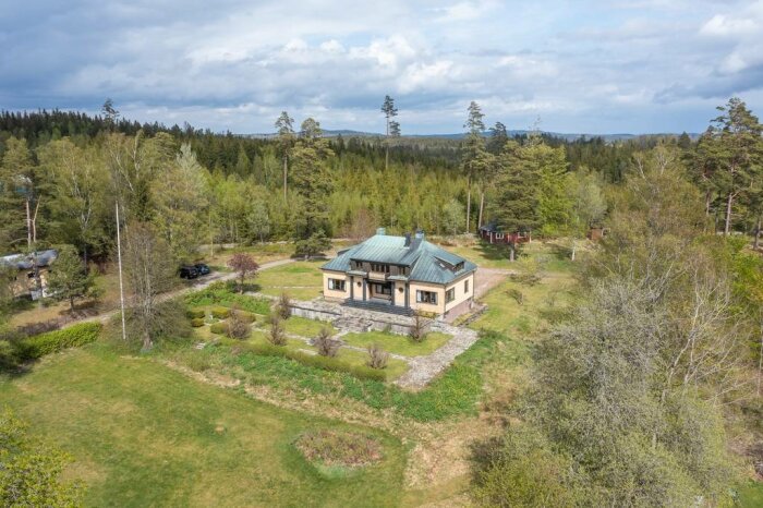 Flygbild över ett stort hus med välansad trädgård omgivet av skog.