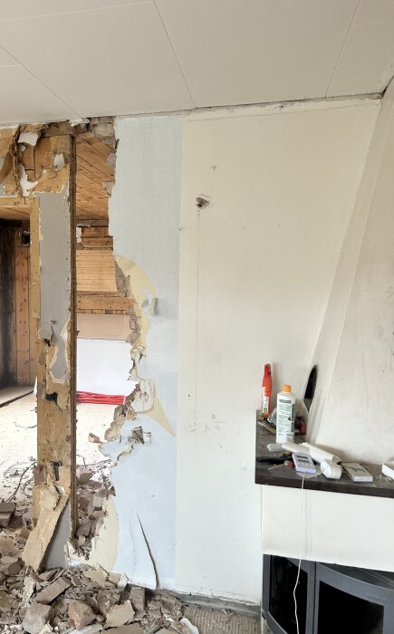 Delvis nedriven vägg med exponerade träbjälkar och tegelskrot på golvet i ett renoveringsprojekt.