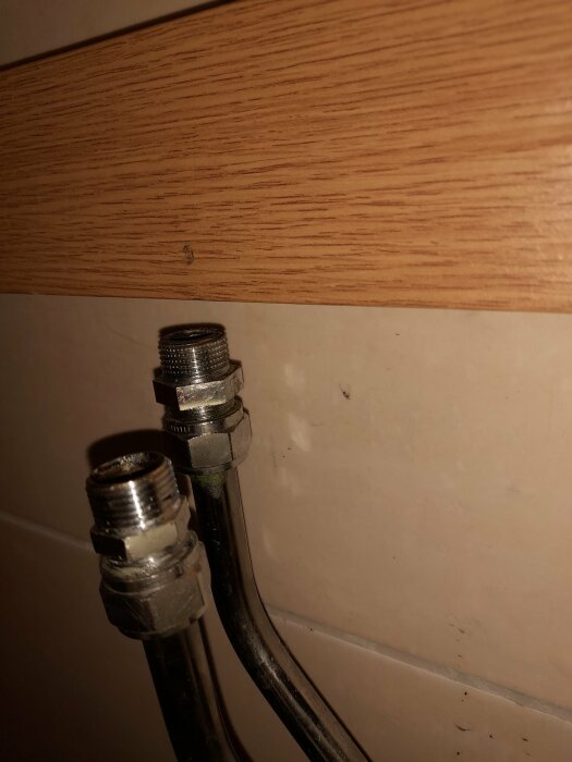 Metallrör med gängade kopplingar under ett trähyllplan, problem vid byte av blandare i badrum.