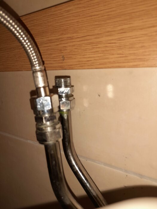 Bild på kopplingen på en gammal blandare under badrumsskåp med synliga vattenledningar och klämringar.