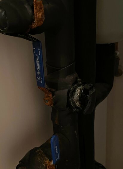 Svart VVS-rör med korrosion och skadad lagningspunkt, omgiven av elband och klämmor.