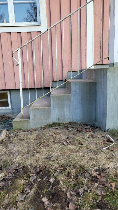 Sliten och skev entrétrappa av betong med ojämna trappsteg framför en husfasad med rosa paneler och ett källarfönster.