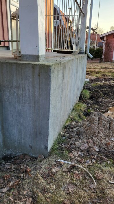 Skev betongtrappa vid husentré med ojämna steg och vitmålad stolpe, behöver renovering.