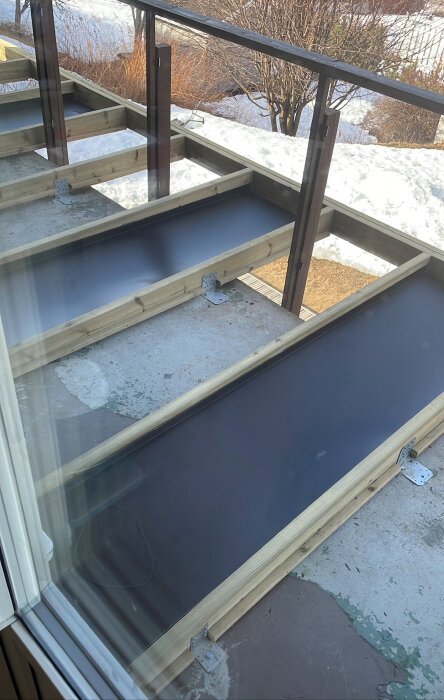 Platt ränna av bockad plåt monterad på balkong med lutning, stött på träribbor, snö och betonggolv syns.