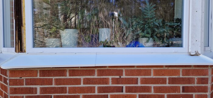 Nyinstallerat fönsterbleck under vit fönsterkarm med synliga ojämnheter och rester av byggmaterial.