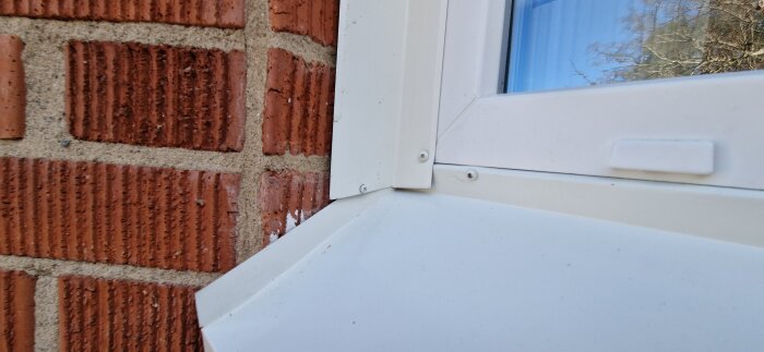 Nyinstallerat vitt fönsterbleck vid tegelvägg med synliga skruvar och ojämna fogar, ifrågasatt monteringskvalitet.