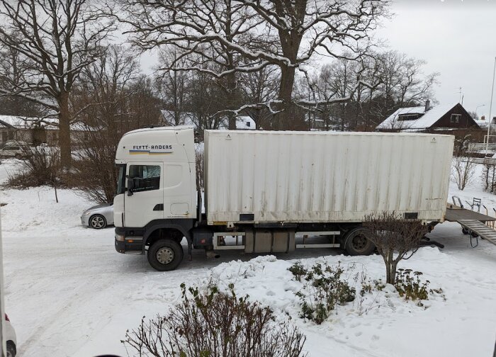 Flyttbil från flyttfirma parkerad utanför hus i snöigt landskap, redo för inflytt.