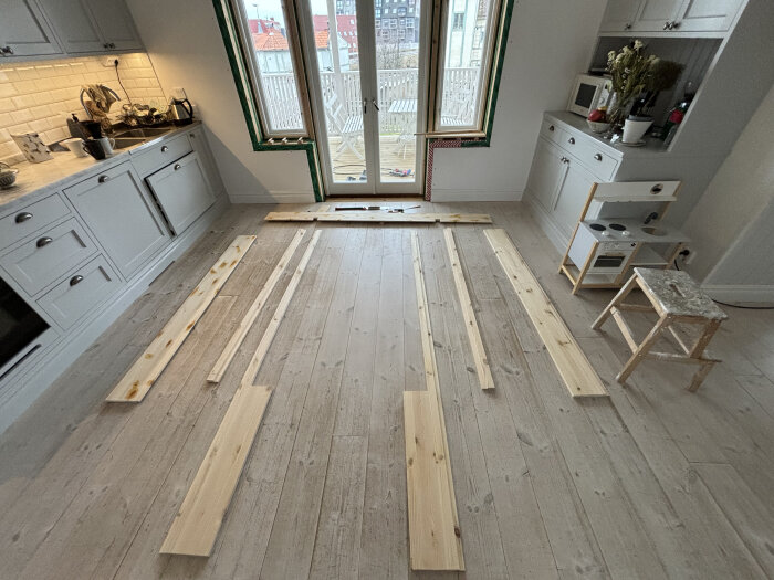 Träribbor utspridda på ett trägolv i förberedelse för fönstersmygens renovering.