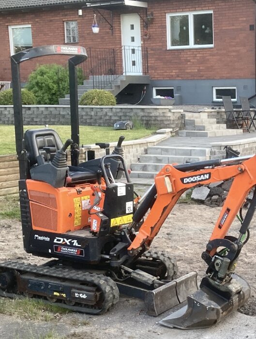 En orange Doosan minigrävare parkerad framför ett tegelhus med renoverad uppfart och trädgård.