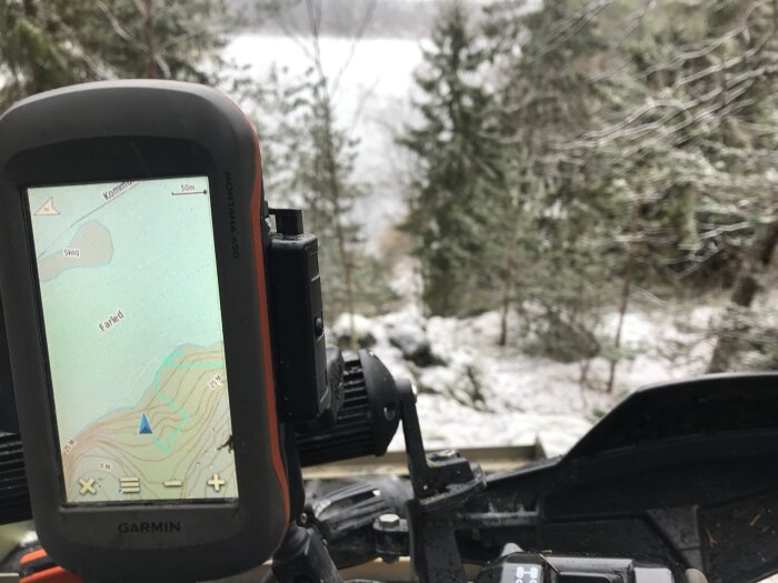 Garmin Montana 650 GPS visar en karta med höjdlinjer monterad på ett fordon med en snöig skog i bakgrunden.