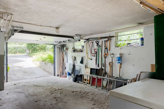 Betonggolv med slitskador i garage med verktyg på väggen och öppen garageport.