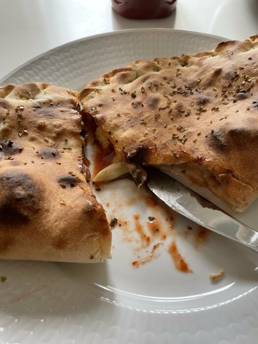 Hemlagad calzone med örter på en vit tallrik, delvis uppäten med synliga fyllningar.