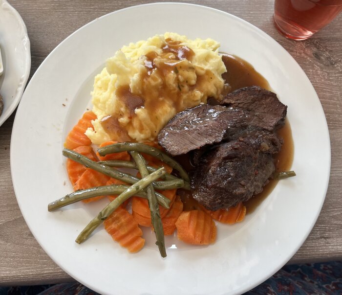 Tallrik med ölbrässerad oxkind, potatismos, skysås och ångade morötter och bönor, serverat med dryck.