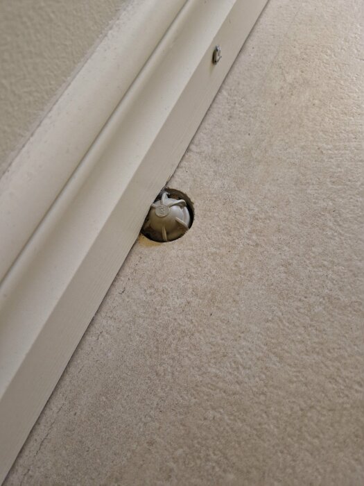 Ventilationslock i ett golv nära en vägg och dörrtröskel, möjlig luftningspunkt för värmesystem.