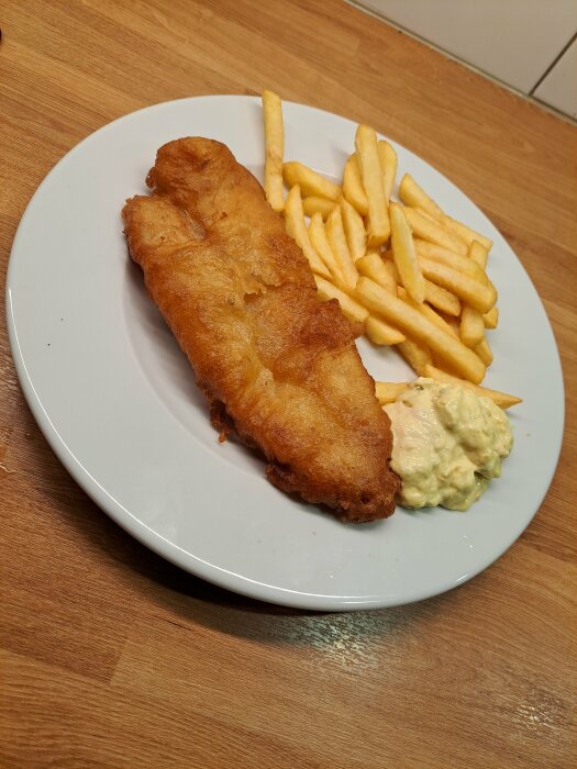 Panerad fiskfilé med pommes frites och remouladsås på en vit tallrik.