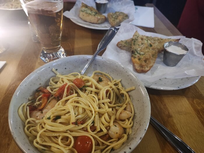 Linguine med räkor i en skål, vitlöksbröd och ölglas med Staropramen på bordet.