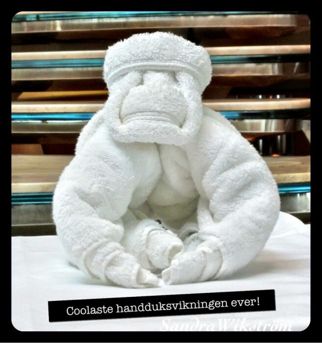 Vit handduk vikt i form av en apa som sitter på en yta med metallräcken i bakgrunden.