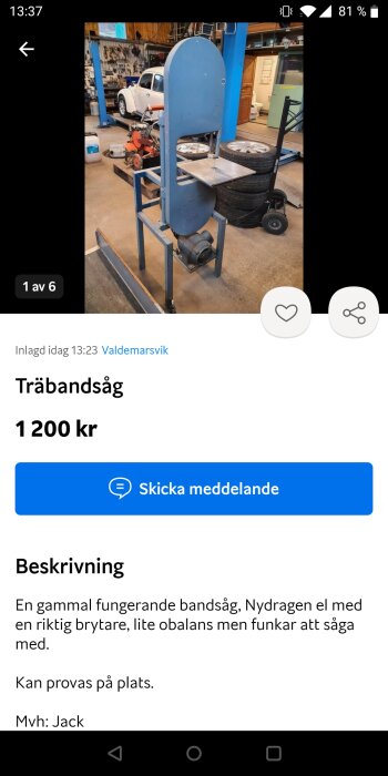 Blå bandsåg i ett verkstadsutrymme med verktyg och bilar i bakgrunden.