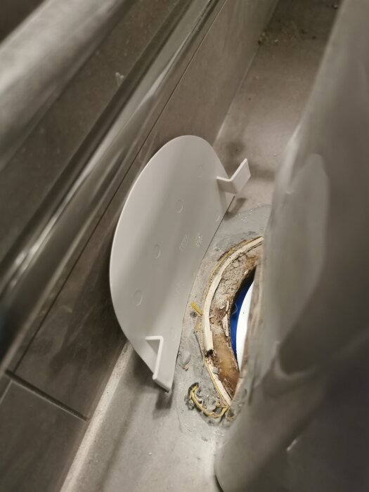 Toalettstol med stor glipa mot avloppshål i badrum, potentiell risk för vattenskador och lukt.