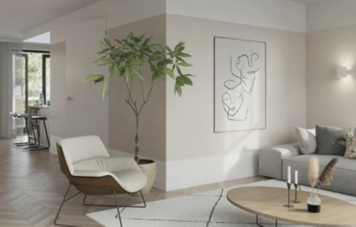 Ett modernt vardagsrum målat i ljusbeige med en bekväm stol, konst på väggen och dekorativa växter.