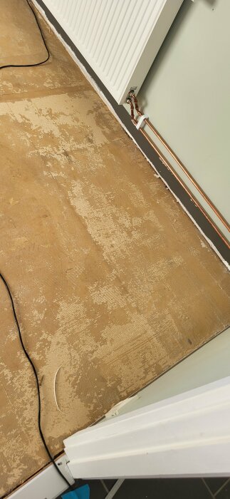 Avlägsnat laminatgolv avslöjar gammalt limmat linoleumgolv och spår av mögel vid en väggkant.