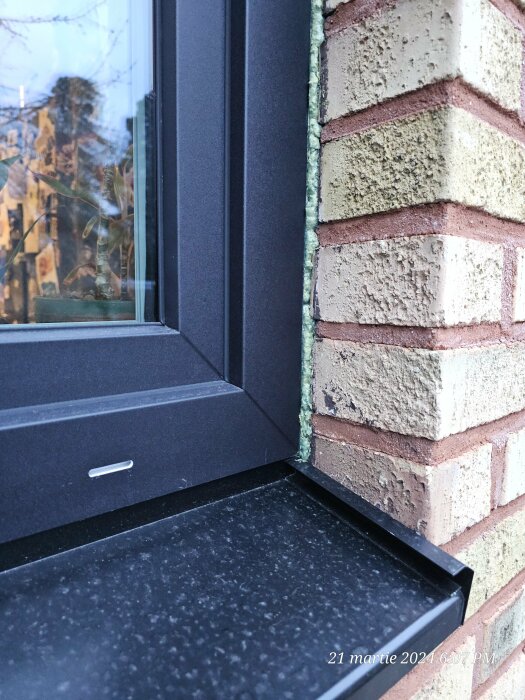 Närbild av ett svart PVC-fönster vid tegelvägg med installerat underbleck.