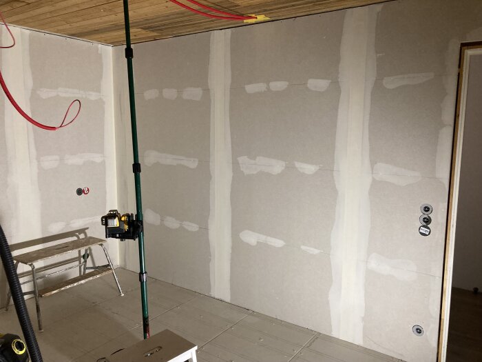 Nyrenoverade väggar med spackel på första lagret, verktyg och bänk synliga i renoveringsrum.