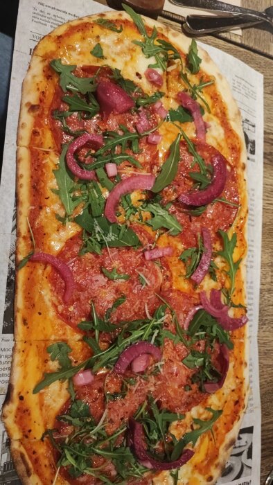 Rustik oval pizza dekorerad med tomatsås, ost, rödlök och rucola från Mocca Deli i Västerås.