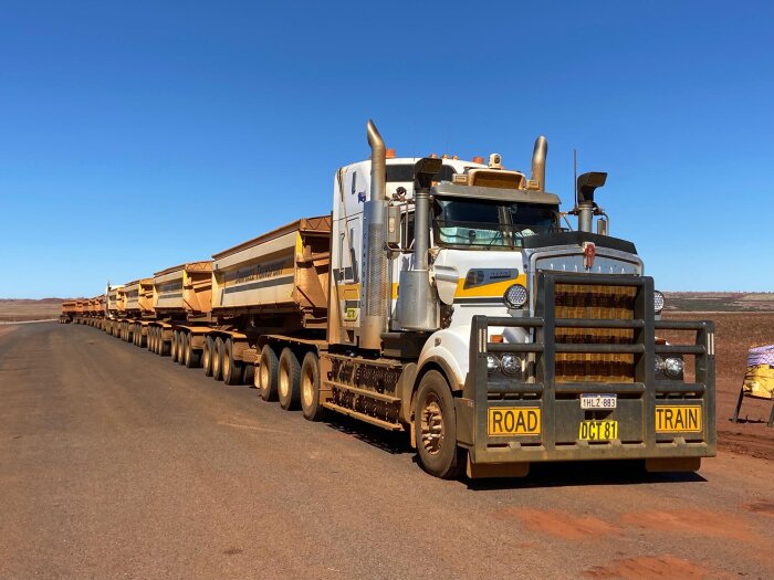 Lastbil med flera släpvagnar, även känd som road train, på en öppen väg i ökenterräng.