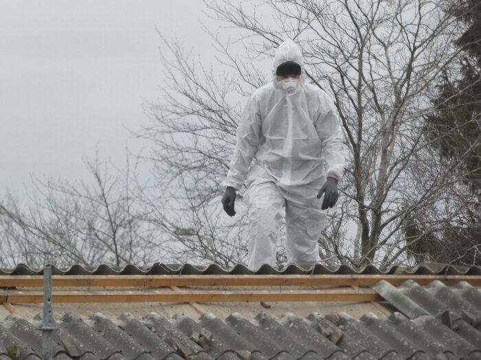 Person i skyddsdräkt och mask på ett tegeltak under renovering.