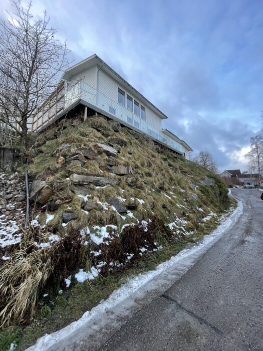 Hus på en höjd med en sluttande tomt och rester av snö, parkeringsutmaning med terräng.