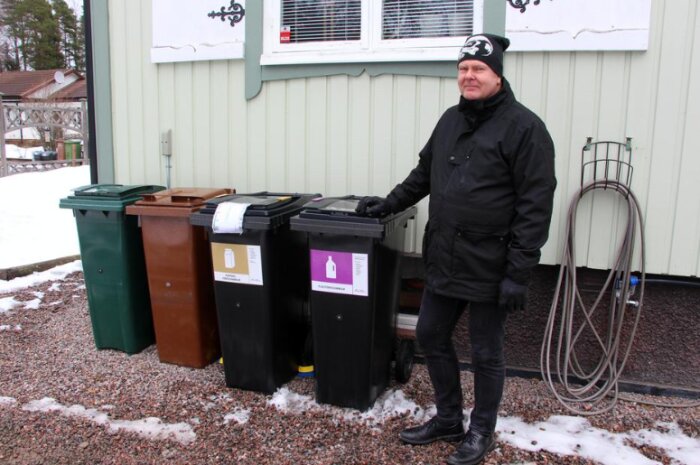 Person står bredvid fyra olika soptunnor för källsortering utomhus i vintermiljö.