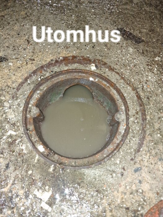 Gammal rostig brunn med texten "Utomhus" och vatten inuti, placerad i en lerig mark.