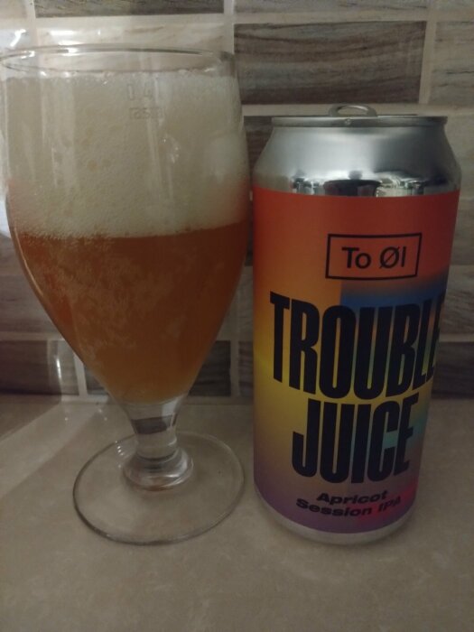 Ett glas öl bredvid en burk med texten "TROUBLE JUICE Apricot Session IPA".