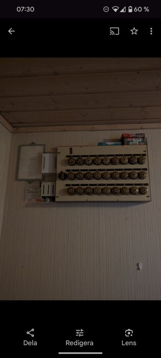 Elcentral med flera säkringar på en beige vägg under ett träpaneltak, med schematiska instruktioner till vänster.