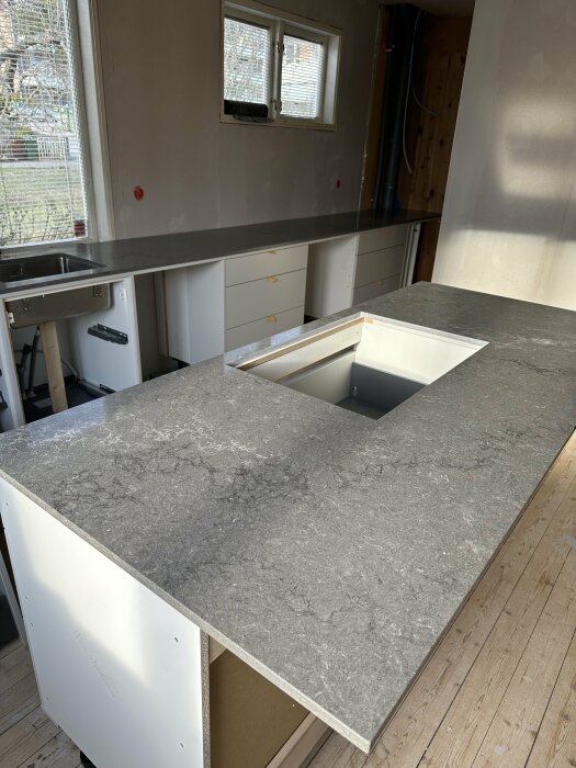 Nymonterad grå bänkskiva i kök med utsågat hål för diskho och vita köksskåp i bakgrunden.