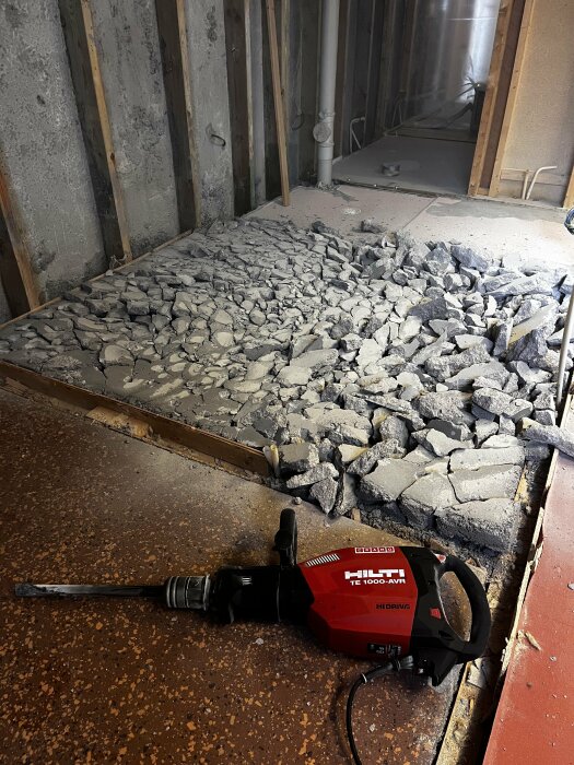 Jackhammer bredvid en hög av sönderslagen betong på ett byggnadsprojekt inomhus.