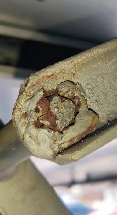 Närbild på en svetsad bult på en metalldörr som spruckit och uppvisar rost och skadad smältmetall.
