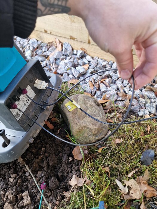 Hand håller ny kabel kopplad till en AM-sändare utomhus med blinkande gult ljus.