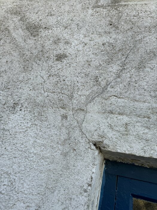Närbild på en spricka i en vitputsad vägg ovanför ett blått fönsterfoder.