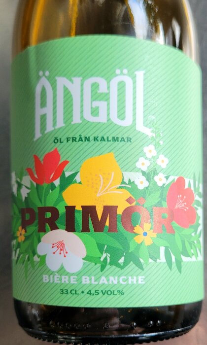 Flaska med lokal veteöl märkt "ÄNGÖL PRIMÖR" och vårblommor på etiketten.