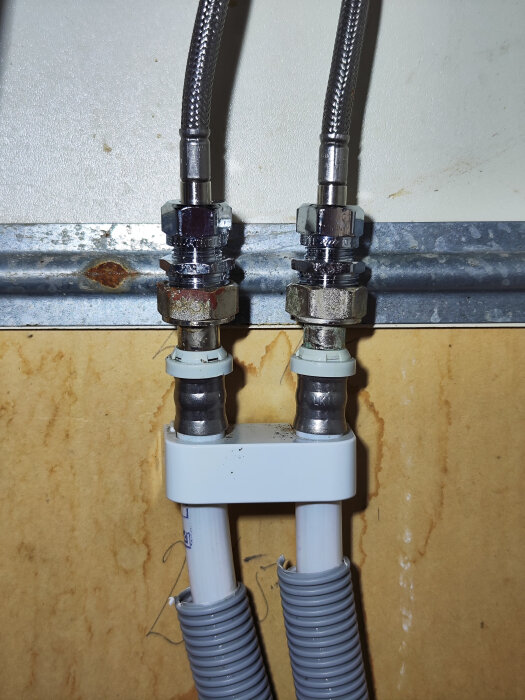 Klämringskoppling installerad på vit rörledning med stålflexslangar och utan kulventil.