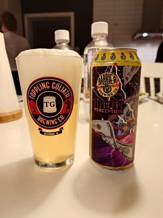 En pint ölglas med skum från Toppling Goliath Brewing och en färgglad Barrier Brewing Co ölburk.