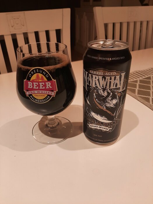 Ölglas med mörkt öl bredvid en burk Barrel-Aged Narwhal Stout på ett vitt bord.