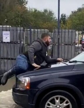 Person hänger på sidan av en bil med öppen dörr och ser ut att försöka ta sig in.